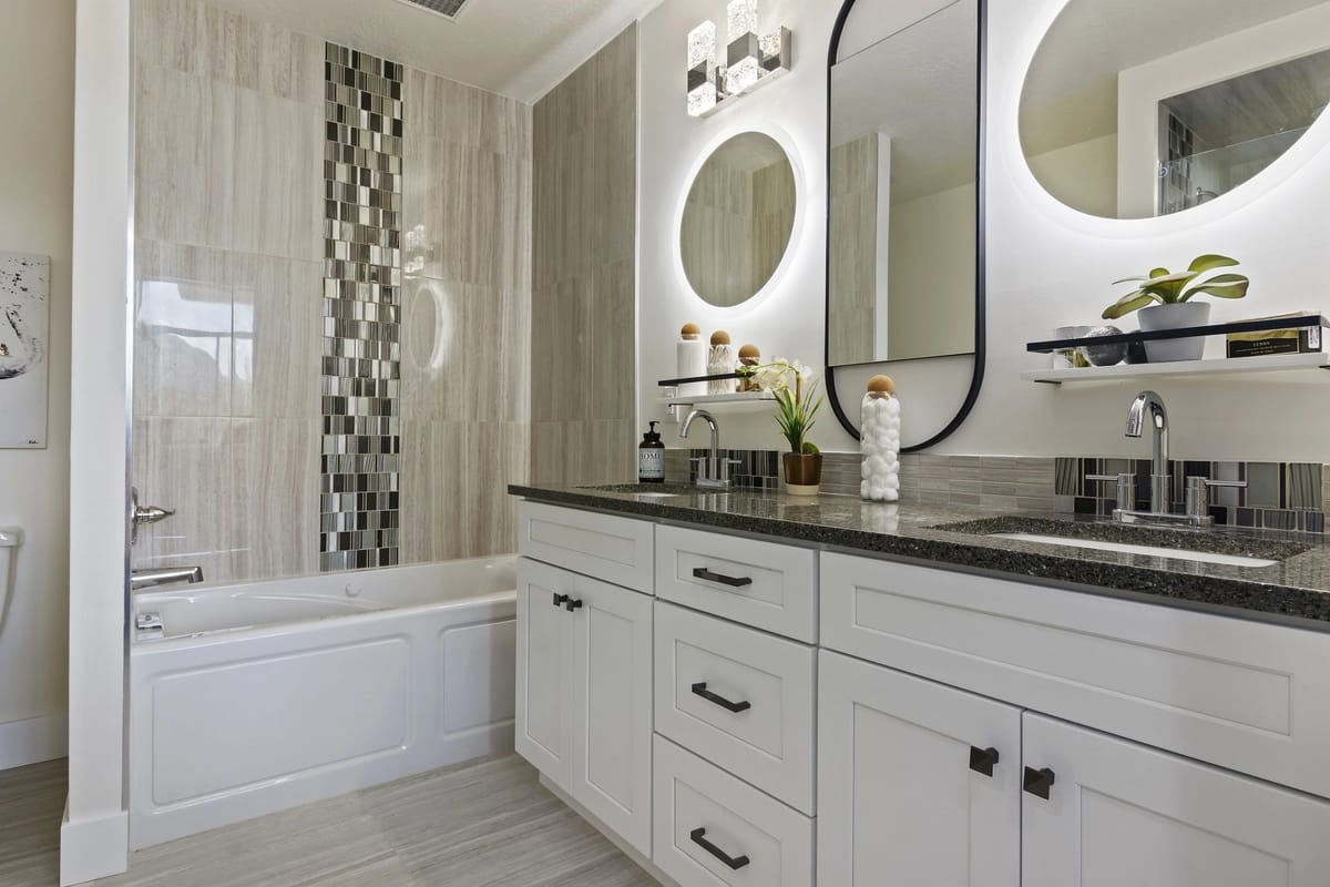 Primary bathroom remodel with a double vanity in white shaker cabinetry, black hardware, granite countertop, two black-framed backlit LED mirrors and a drop-in soaking tub with a vertical glass mosaic tile inlay.