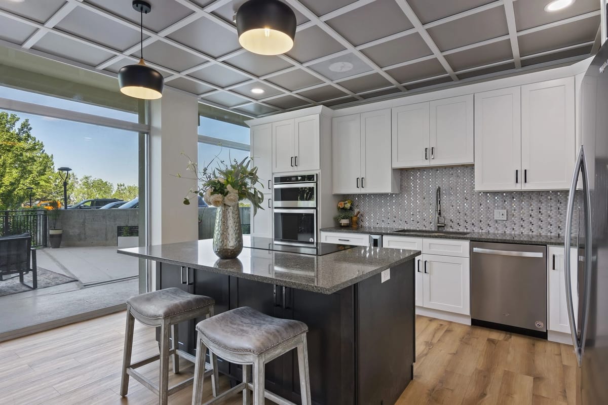 Remodelled kitchen with white shaker cabinets, a charcoal island with granite countertop, black drum pendant lights and a grey coffered ceiling, opening onto a covered patio through full-height sliding glass doors.